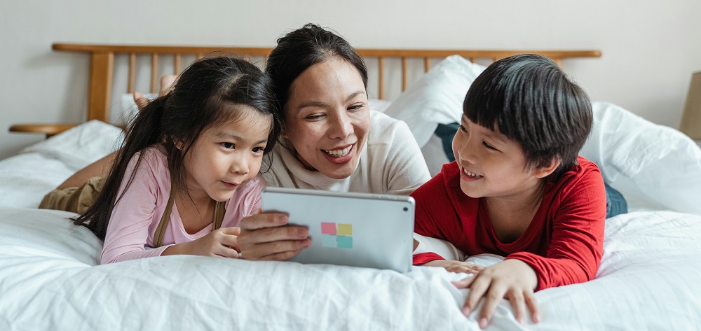 Parent watching a video on a tablet with her children by Ketut Subiyanto